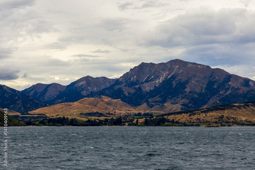 Lake Wanaka, a summer cloudy afternoon with a mountain range and the town of Wanaka on the shore. South Island, New Zealand