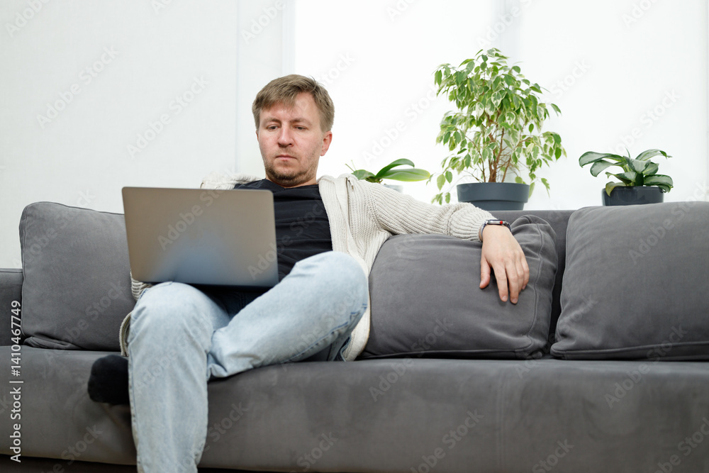 Man on sofa in living room working on laptop Man on sofa in living room working on laptop