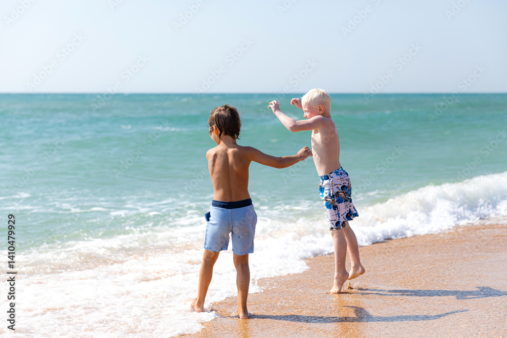 Happy children, two little boys, enjoy summer vacation near the sea, play on sandy beach, have fun. Advertising for tour operators, hotels, airlines. Childhood, happiness and freedom concept.