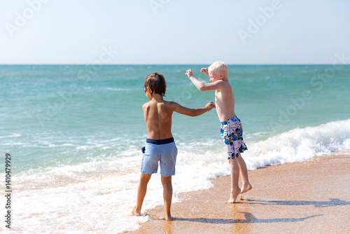 Obraz na płótnie Happy children, two little boys, enjoy summer vacation near the sea, play on sandy beach, have fun. Advertising for tour operators, hotels, airlines. Childhood, happiness and freedom concept. w salonie
