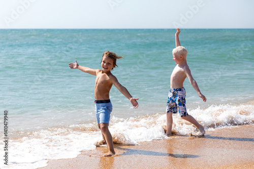 Obraz na płótnie Happy children, two little boys, enjoy summer vacation near the sea, play on sandy beach, have fun. Advertising for tour operators, hotels, airlines. Childhood, happiness and freedom concept. w salonie