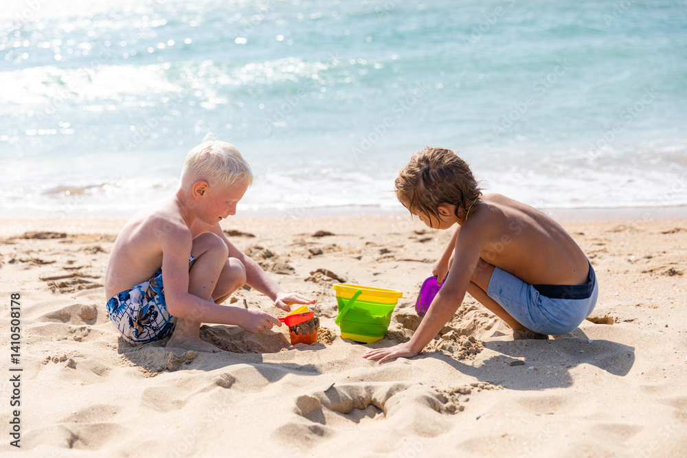 Children two little boys playing on the beach on summer holidays. Children having fun with a sand on the seashore. Vacation concept. Happy sunny day. Joyful children with beautiful sea, sand