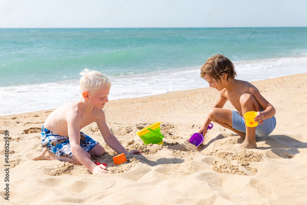 Children two little boys playing on the beach on summer holidays. Children have fun, build sand castle on the seashore. Vacation concept. Happy sunny day. Happy kids with ocean background. Copy space