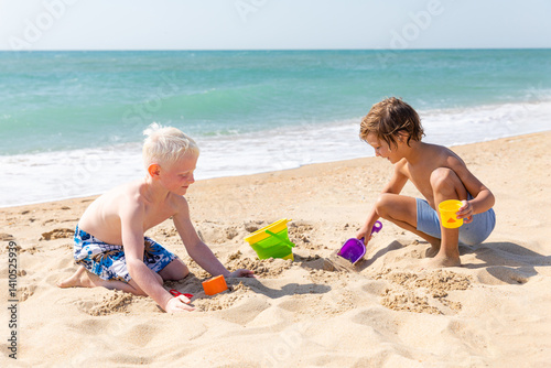 Obraz na płótnie Children two little boys playing on the beach on summer holidays. Children have fun, build sand castle on the seashore. Vacation concept. Happy sunny day. Happy kids with ocean background. Copy space w salonie