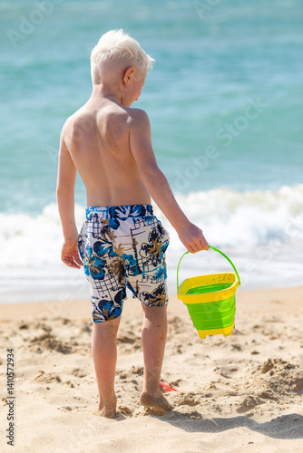 Happy little boy holding beach sand bucket. Concept of children beach summer vacation. High quality photo