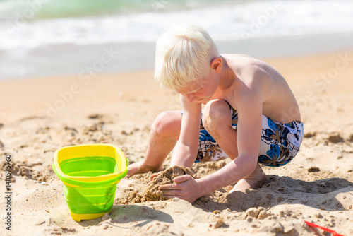 Obraz na płótnie Happy child little boy playing with the sand on the beach, building sand castle, enjoying summer, playing. Advertising for tour operators, hotels, airlines. Vacation concept. w salonie