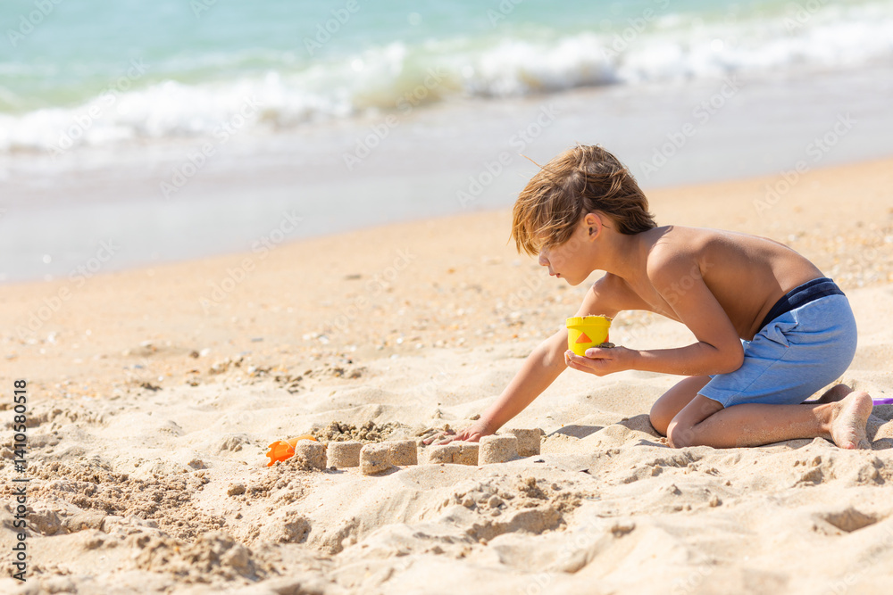 Side view child little boy playing with the sand on the beach, building sand castle, enjoying summer, playing. Advertising for tour operators, hotels, airlines. Vacation concept.
