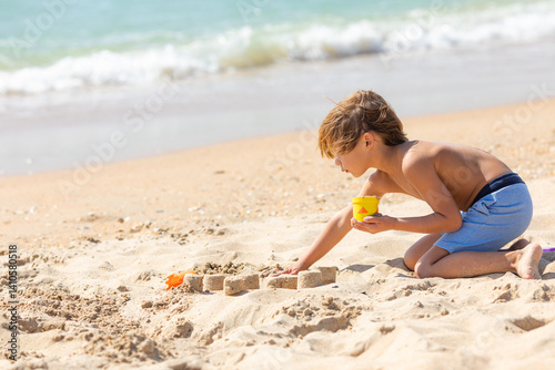 Obraz na płótnie Side view child little boy playing with the sand on the beach, building sand castle, enjoying summer, playing. Advertising for tour operators, hotels, airlines. Vacation concept. w salonie