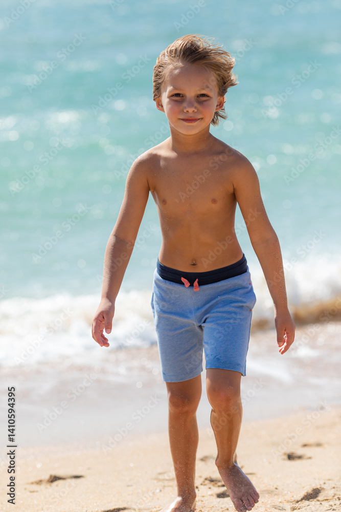 Cute little boy playing on the beach on summer holidays. Joyful child in nature with beautiful sea, sand and blue sky. Happy kid on vacations at seaside running in the water and having fun