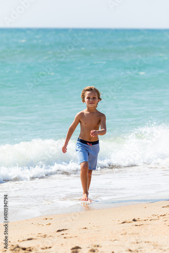 Obraz na płótnie Cute little boy playing on the beach on summer holidays. Joyful child in nature with beautiful sea, sand and blue sky. Happy kid on vacations at seaside running in the water and having fun w salonie