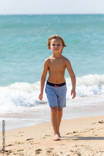 Obraz na płótnie Cute little boy playing on the beach on summer holidays. Joyful child in nature with beautiful sea, sand and blue sky. Happy kid on vacation, walking on the beach and having fun w salonie