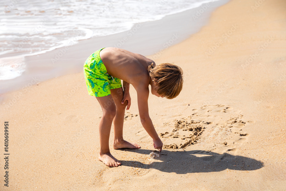 Cute little boy playing on the beach on summer vacation, writing on a sand. Joyful child in nature with beautiful sea and sand background. High quality photo