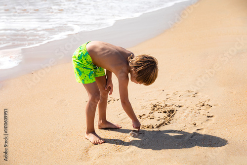 Obraz na płótnie Cute little boy playing on the beach on summer vacation, writing on a sand. Joyful child in nature with beautiful sea and sand background. High quality photo w salonie