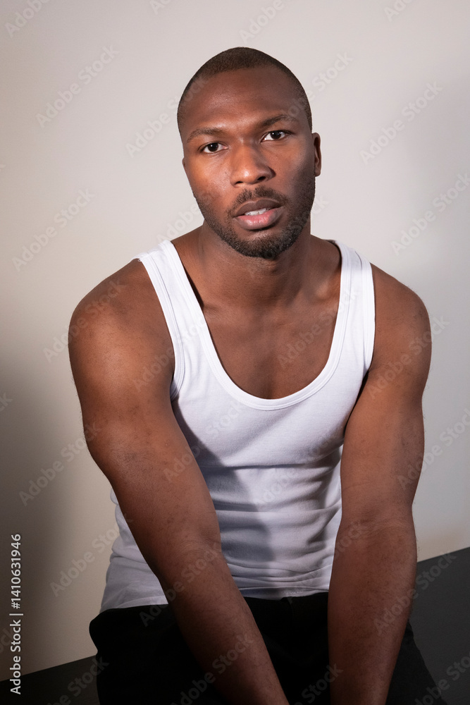 Fototapeta premium A man in a white tank top sitting with his arms folded and looking ahead