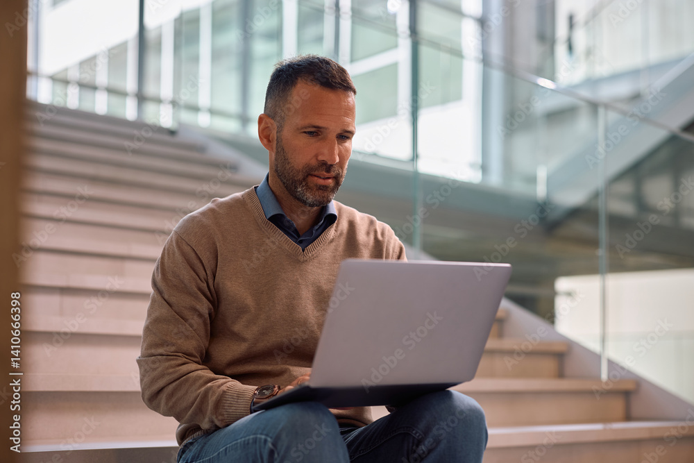 Fototapeta premium Corporate manager using laptop on staircase of office building.