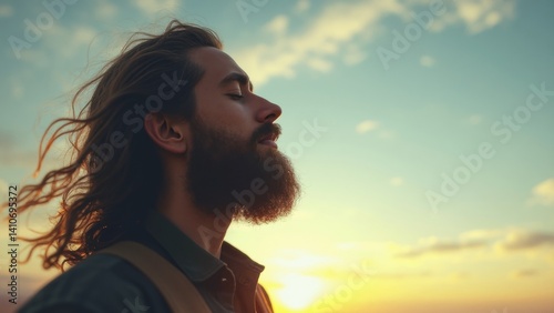 Obraz na płótnie Man with a beard and long hair is looking up at the sky. The sky is blue and the sun is setting. The man is in a peaceful and contemplative mood w salonie