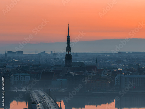 Obraz na płótnie Serene sunrise over Riga, Latvia, featuring St. Peter's Church spire, a bridge over the Daugava River, and reflections in calm water with morning mist. w salonie