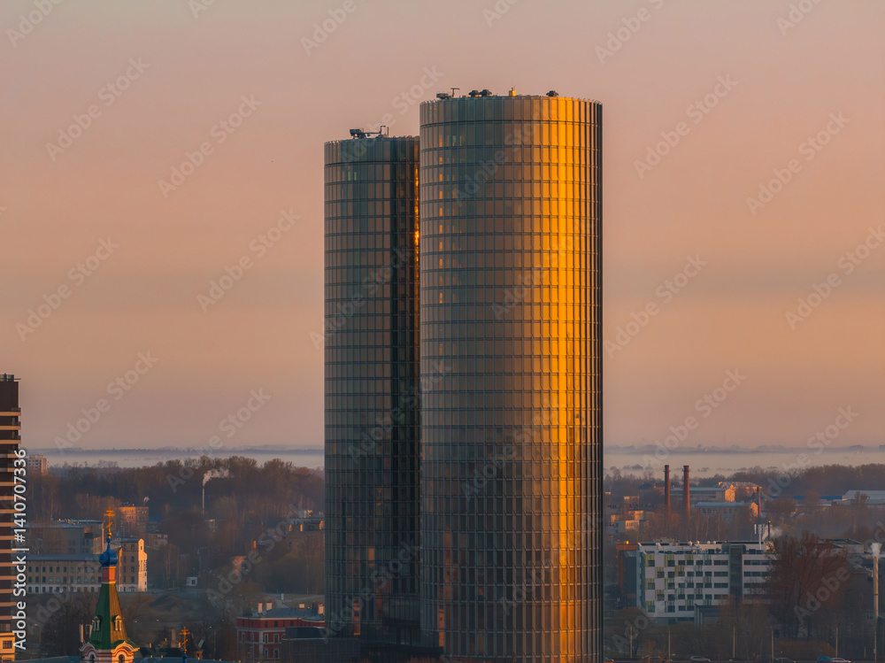 Serene sunrise over Riga, Latvia, featuring the reflective Z Towers, urban structures, a church spire, and a faintly visible river in the background.