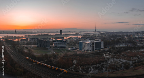Obraz na płótnie Serene sunrise in Riga, Latvia, featuring the Riga TV Tower, Daugava River, modern buildings, a yellow train, and historic spires in the distance. w salonie