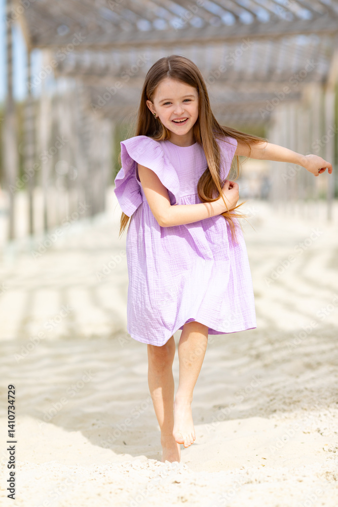 Carefree summer. Little girl in lilac dress has fun and running barefoot on sandy beach under wooden gazebo on sunny day. Joyful childhood adventures and tropical vacation concept. Space for text. Carefree summer. Little girl in lilac dress has fun and running barefoot on sandy beach under wooden gazebo on sunny day. Joyful childhood adventures and tropical vacation concept. Space for text.