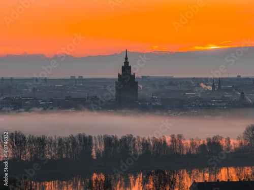 Obraz na płótnie A vibrant sunrise over Riga, Latvia, with the Latvian Academy of Sciences in view, mist covered cityscape, and the Daugava River reflecting warm hues. w salonie