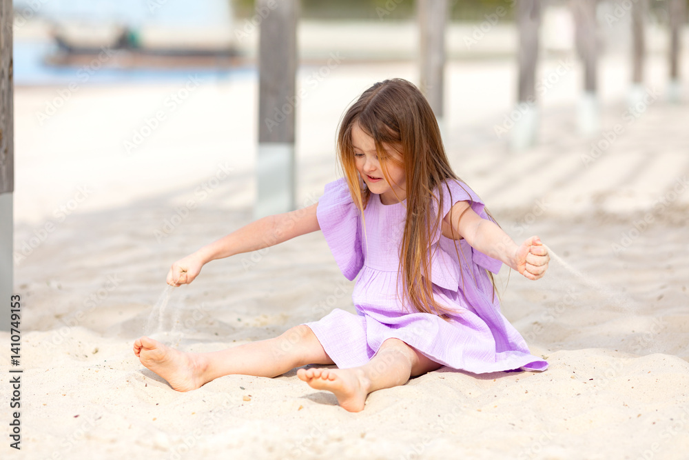 Little cute child girl sitting on tropical beach and playing with sand, smiling on summer vacation. Happy children kid enjoy and has fun. Outdoor activity lifestyle on beach, holiday travel.