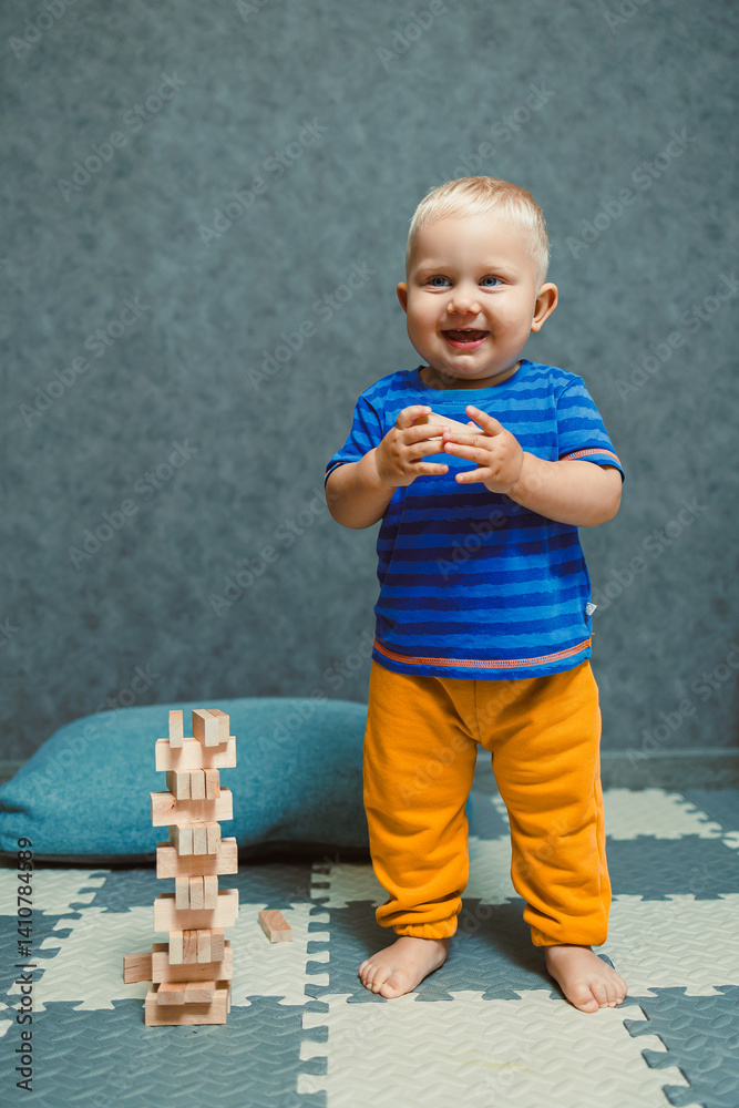 One-year-old boy running around the nursery at home. Toddler boy in a T-shirt and pants playing with toys at home. Children's home clothes. Child's self-development at home.
