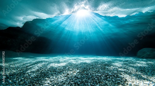 Beneath the ocean's surface, light filters through the water, illuminating a tranquil underwater landscape filled with shimmering pebbles and captivating hues of blue.