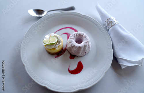 Gala gourmet desserts. Top view of a lemon curd over quiche, with meringue, berries ice cream and sauce, in a white dish with an elegant table setting