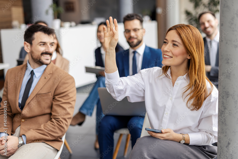 A businesswoman sitting at training room with hand raised and asking questions.