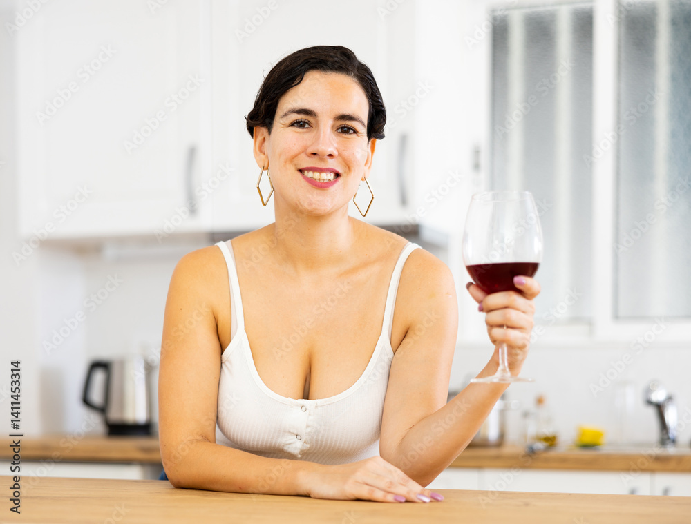 Smiling young hispanic woman relaxing after work at home, leaning on table in kitchen with glass of wine Smiling young hispanic woman relaxing after work at home, leaning on table in kitchen with glass of wine