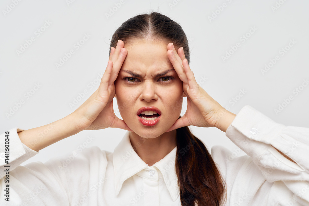woman expressing frustration, holding her head, wearing a white shirt on a light gray background, showcasing emotions of stress and annoyance in a simple, minimalistic setting