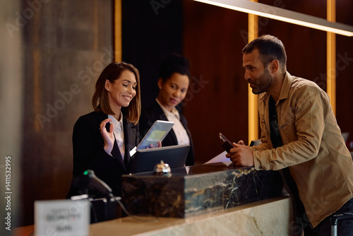 Happy female receptionist using touchpad while welcoming guest in hotel. photo