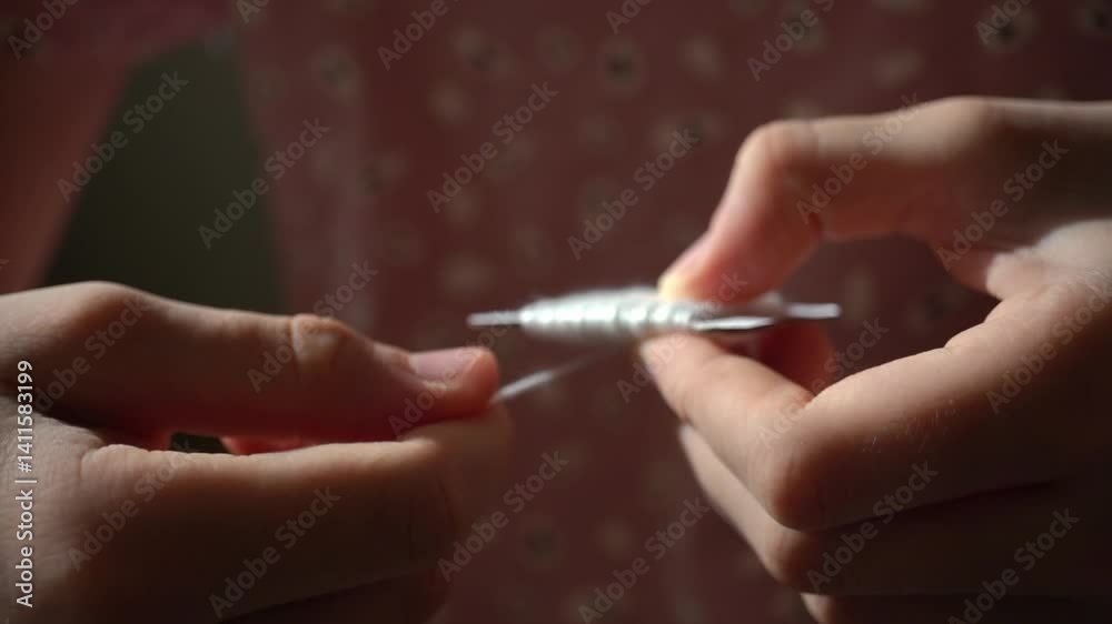 Textile detail: a spool of embroidery floss with white threads in a child's hands. Preparing for embroidery. Close-up of a girl's hands winding white floss onto a spool Textile detail: a spool of embroidery floss with white threads in a child's hands. Preparing for embroidery. Close-up of a girl's hands winding white floss onto a spool