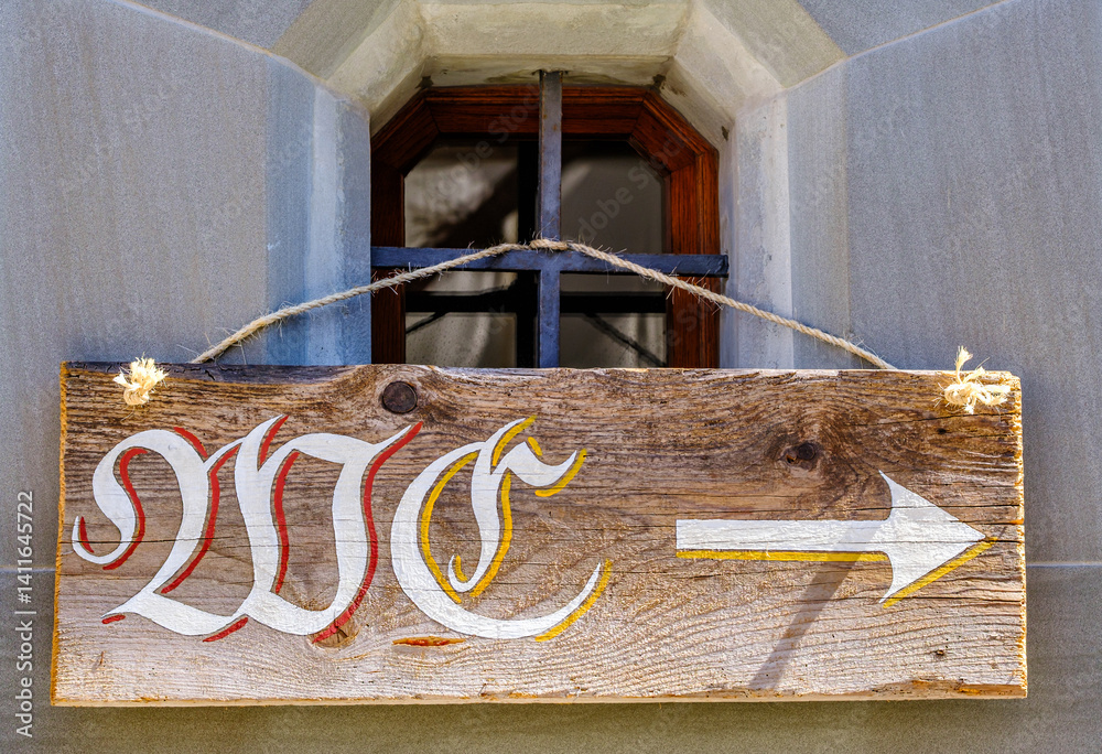 Rustic wooden sign with directional arrow indicating location in a historical building near a window on a sunny day