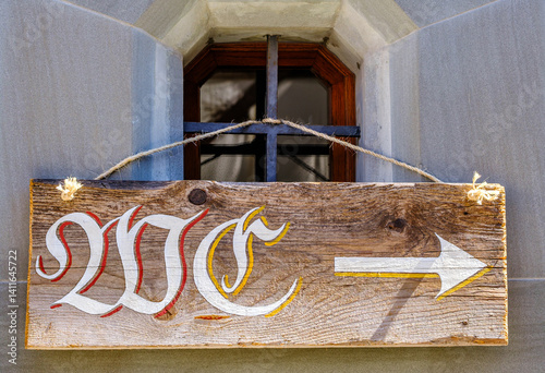 Obraz na płótnie Rustic wooden sign with directional arrow indicating location in a historical building near a window on a sunny day w salonie