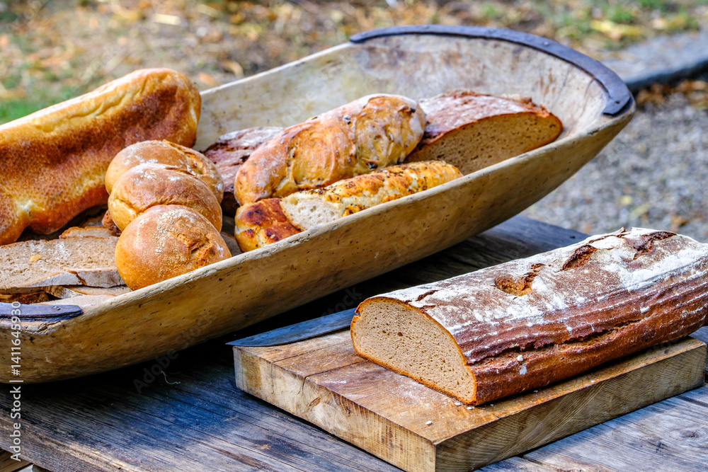 Freshly baked medieval breads displayed on a wooden table with a large basket in a rustic outdoor setting