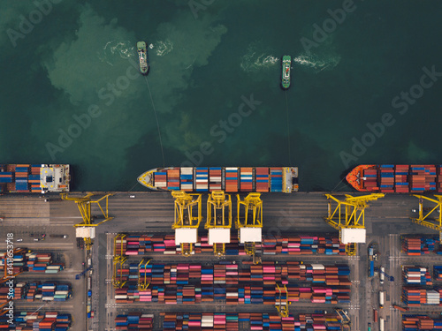 Aerial top view over international containers cargo ship at industrial import-export port prepare to load containers with big container loader ship vessel. global transportation and logistic business.