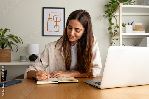Young happy woman handwriting on a notebook while working at home office. Female college student doing homework
