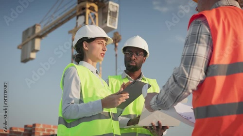 Wallpaper Mural Male and female engineers discussing blueprints, analyzing data, holding tablet, rooftop with cranes. Team collaborating, sharing ideas, reviewing plans, under clear sky near construction site. Torontodigital.ca