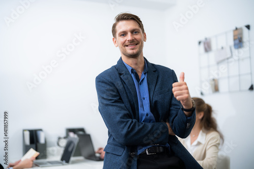 Professional man smiling and giving a thumbs up in modern office during a team meeting
