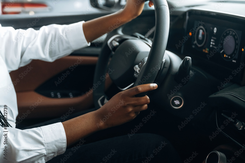 Naklejka premium Two hands are on the steering wheel. Woman in white shirt is in the modern car