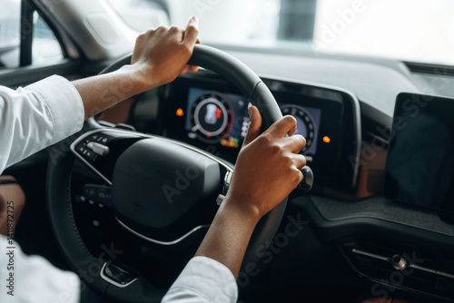 Two hands are on the steering wheel. Woman in white shirt is in the modern car