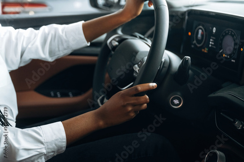 Two hands are on the steering wheel. Woman in white shirt is in the modern car