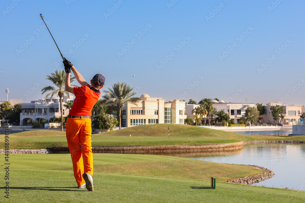 Obraz premium Golfer taking swing on luxury waterfront course, Male golfer in bright outfit swinging club on a high-end golf course near water.