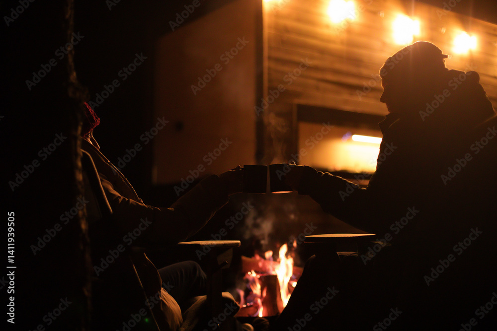 A cozy nighttime scene of two people sitting by a fire, clinking mugs in celebration. Warm lighting, steam rising from the cups, and a peaceful outdoor atmosphere create a relaxing vibe.