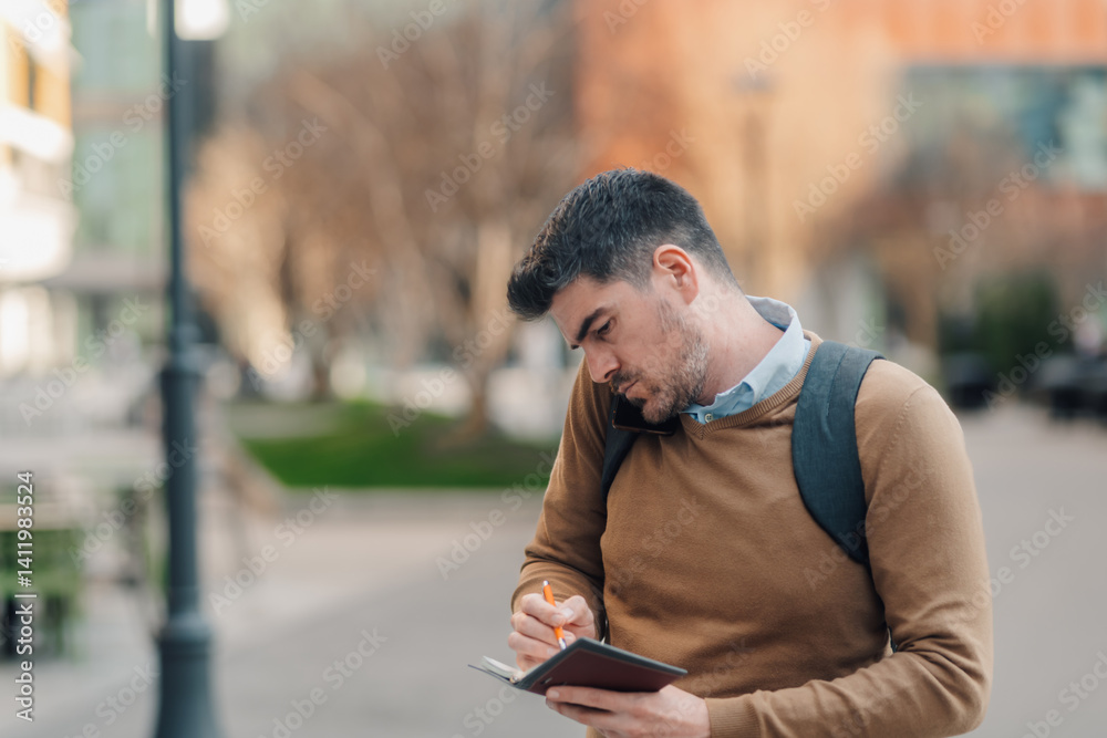 Businessman writing notes while talking on phone in urban setting Businessman writing notes while talking on phone in urban setting