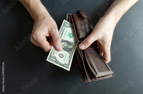 man takes out the last 1 dollar bill from his wallet. abstraction on the topic of high cost of living and bankruptcy
