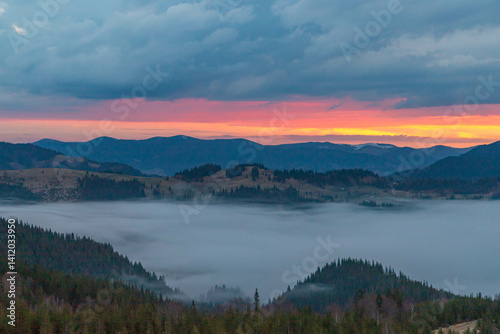 Fototapeta Naklejka Na Ścianę i Meble -  dawn in the mountains, clouds cover the foot of the mountains, orange sky and gray clouds