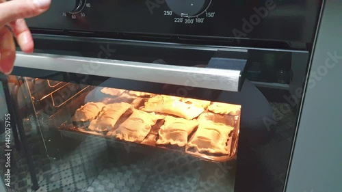 Person places baking tray with pastries into the oven. Baking